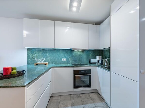 A modern kitchen with white cabinets, a green marble backsplash, and a built-in oven.