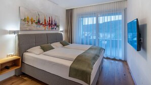 A modern bedroom with a large bed, a mounted TV, and a painting of sailboats. - Seeblick alpe maritima Ski & See-Top 12 by Interhome (Ossiacher See)