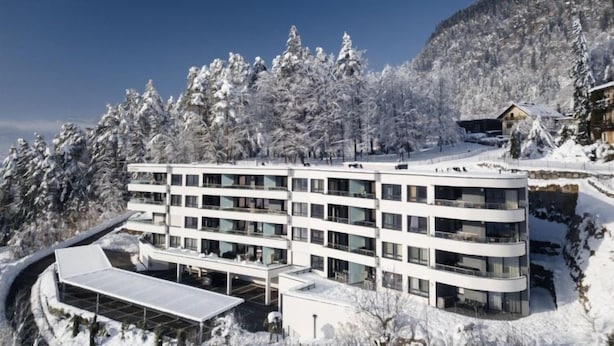 A modern multi-story hotel with a flat roof, surrounded by snow-covered trees and a mountainous backdrop. - Seeblick alpe maritima Ski & See-Top 12 by Interhome (Ossiacher See)