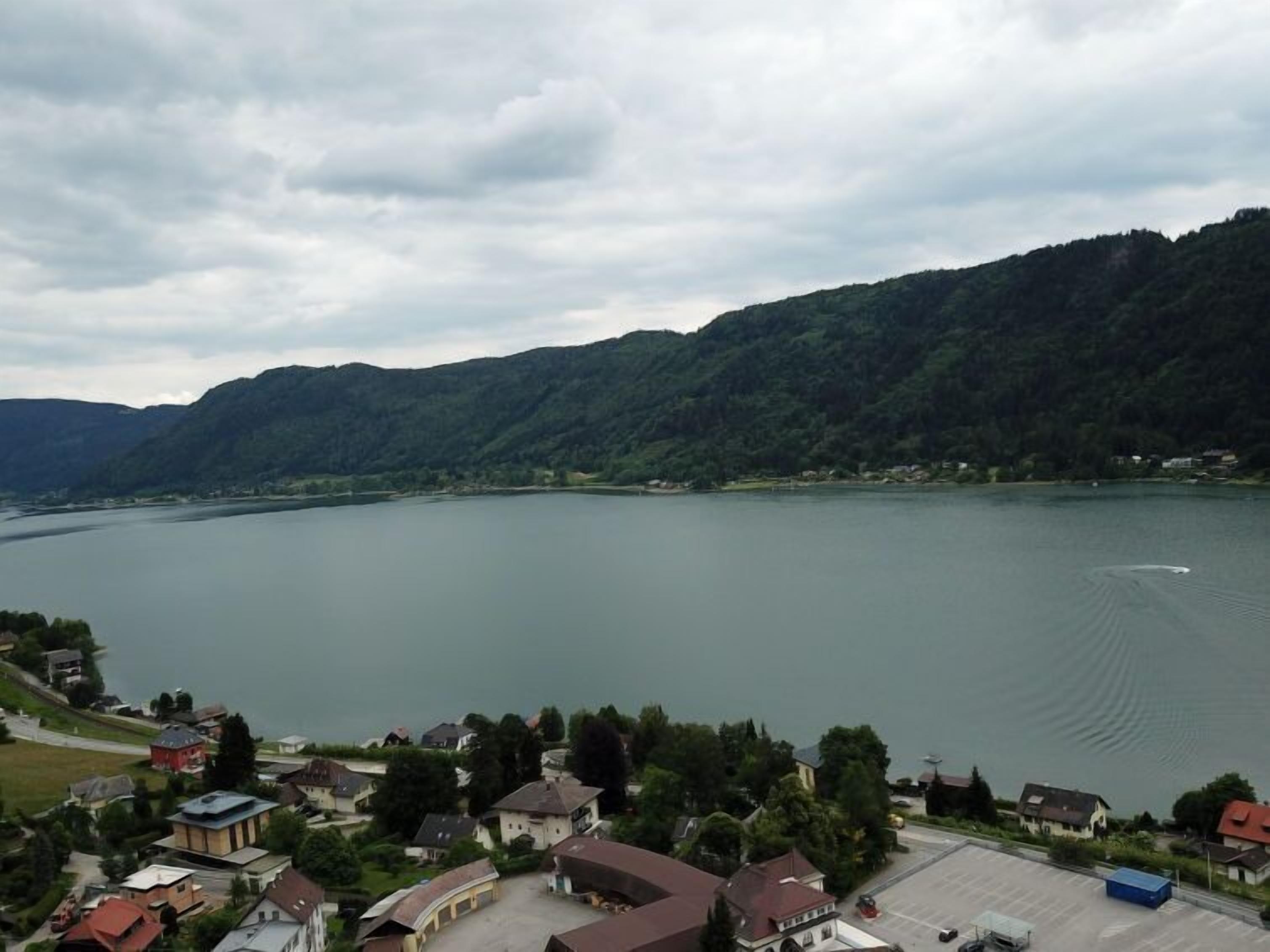 Un pueblo a orillas de un lago, con casas e iglesia, rodeado de colinas.