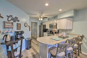 A modern kitchen with a central island, bar stools, a coffee station, and a 'Welcome' sign. - Ethel's Beachfront Retreat (Wisconsin Dells)