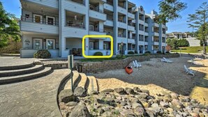 Ett hotell med flera våningar och balkonger, en sandstrand med solstolar och en stenlagd gångväg som leder till entrén.