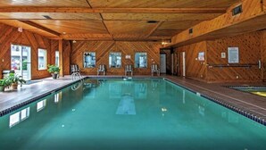Une grande piscine intérieure aux murs et au plafond en bois, entourée de chaises longues et de plantes en pot.
