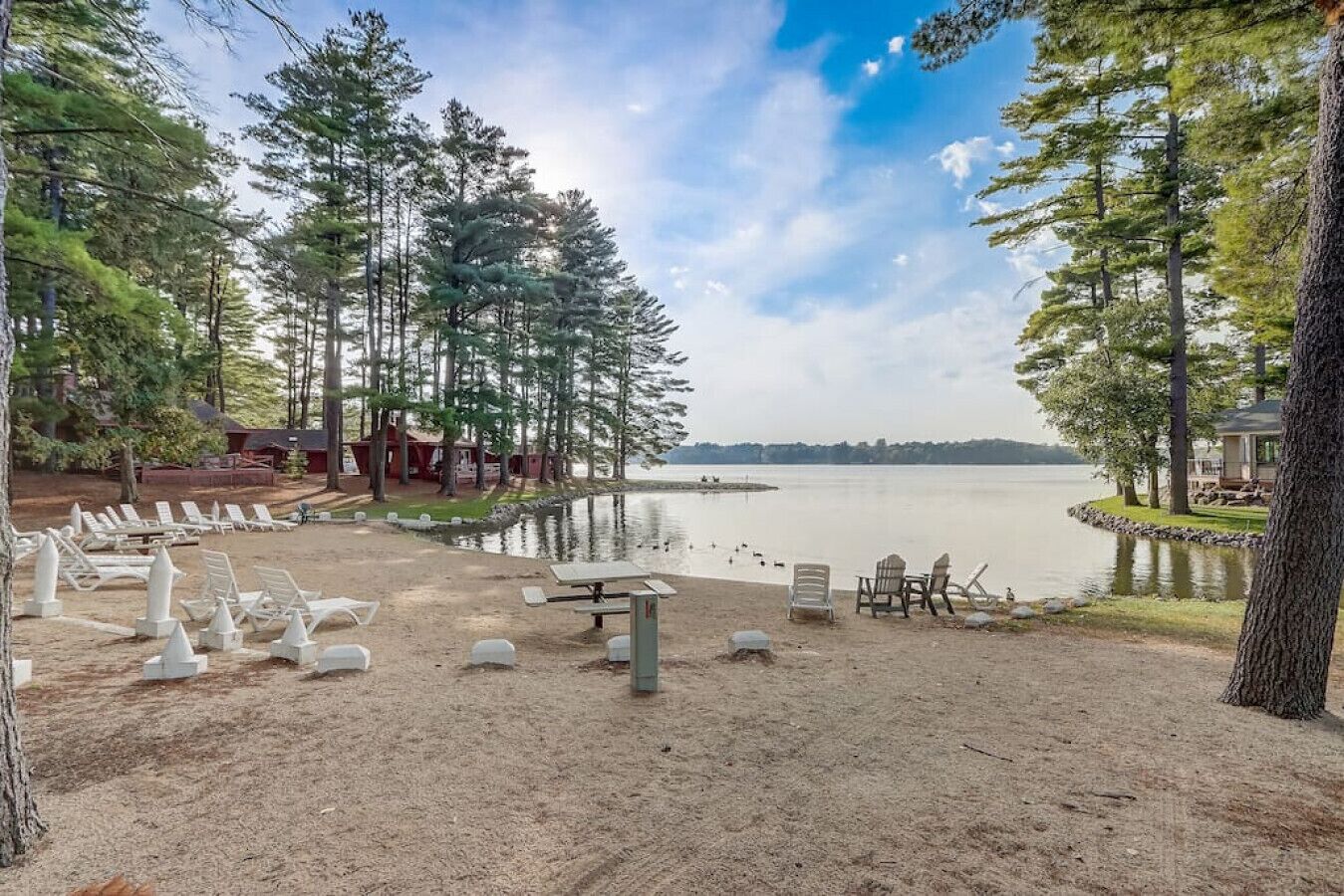 A lakeside campsite with lounge chairs, a picnic table, and cabins in the background.