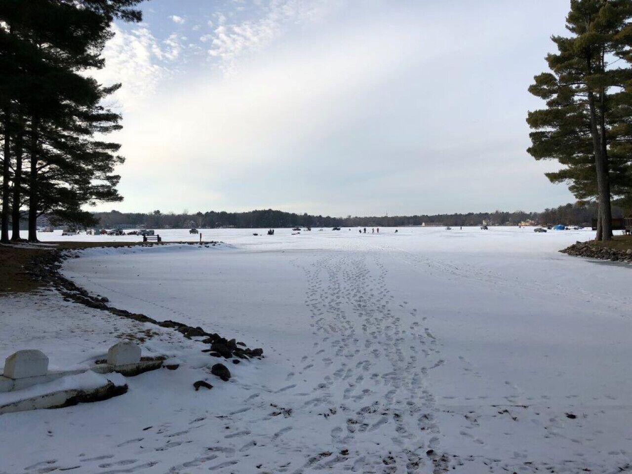 Een sneeuwbedekt strand met voetafdrukken die naar het water leiden, omringd door bomen.