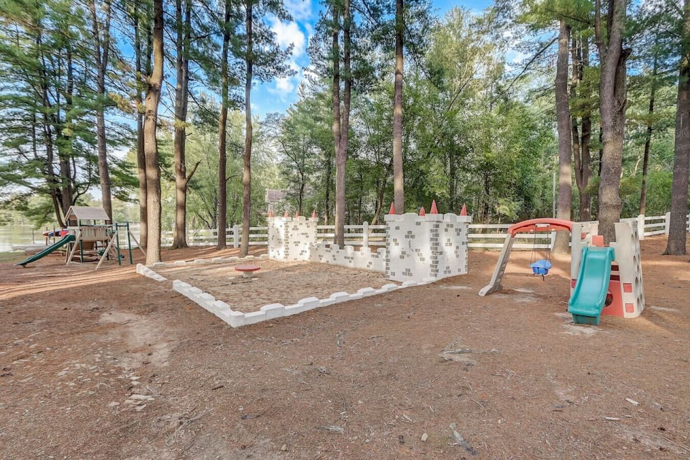 A playground with a slide, swings, and a climbing structure surrounded by trees.