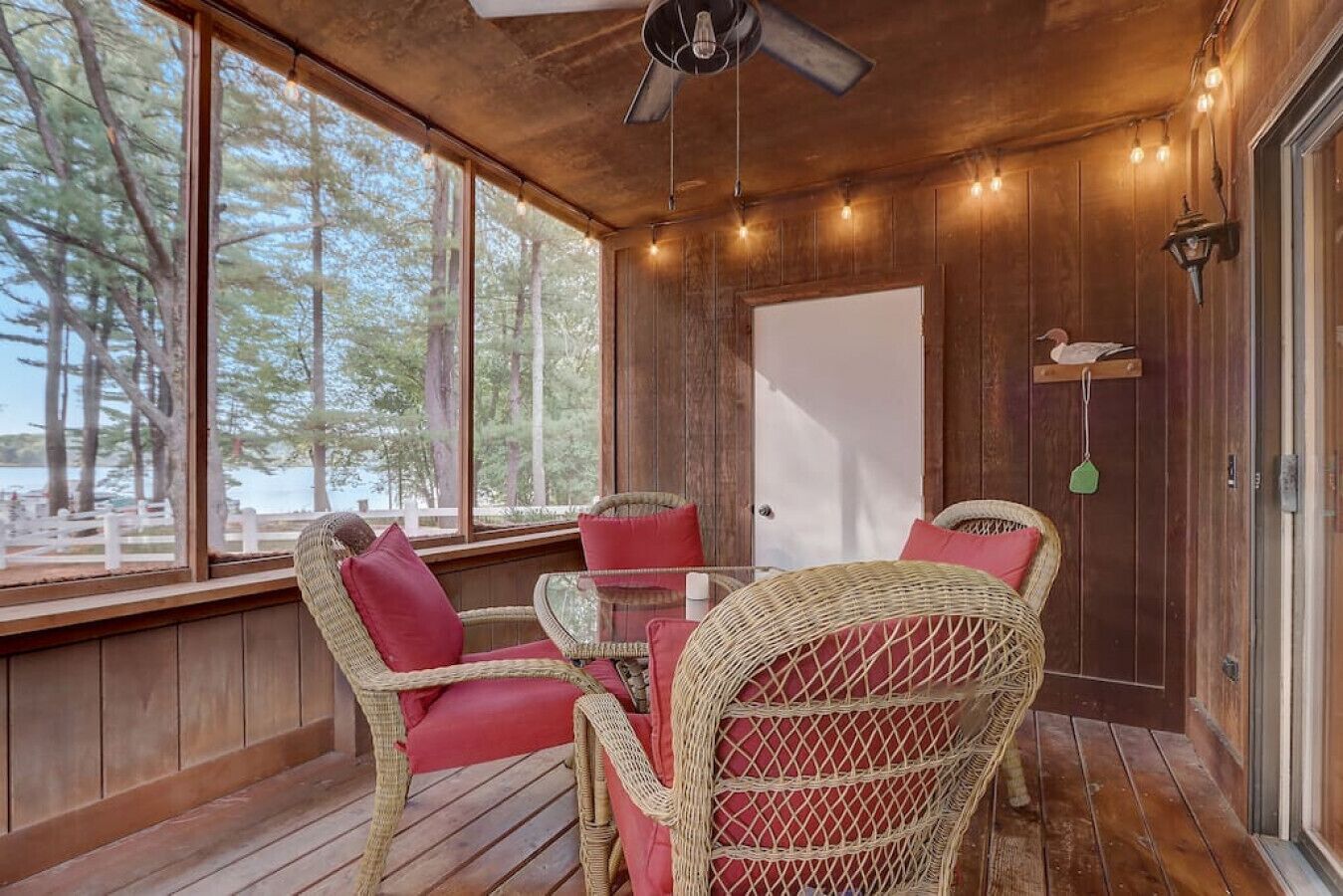 A wooden deck with wicker chairs and a glass table, overlooking a lake.
