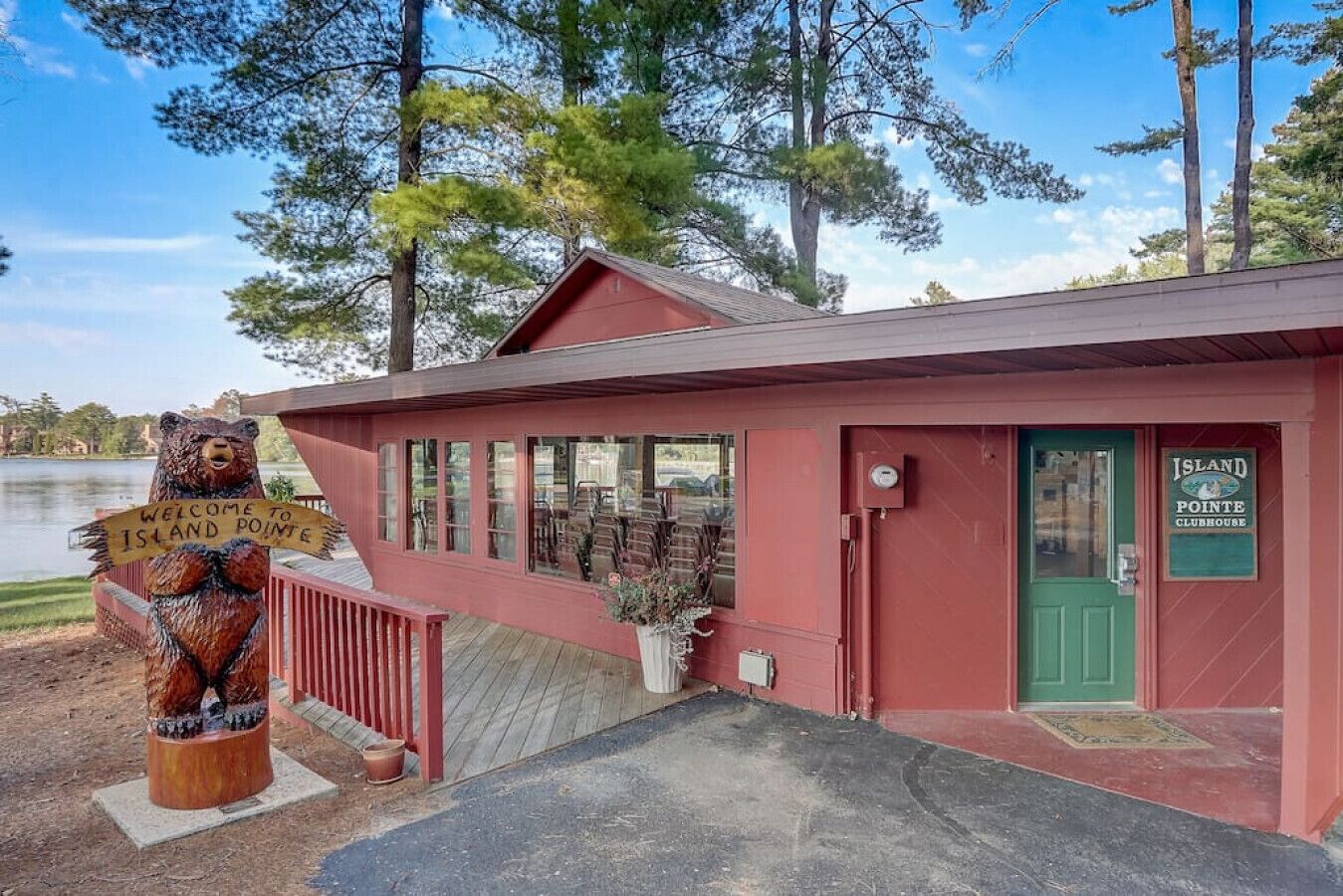 A red building with a green door, a sign reading "Island Pointe Clubhouse," and a wooden bear statue with a sign saying "Welcome to Island Pointe."