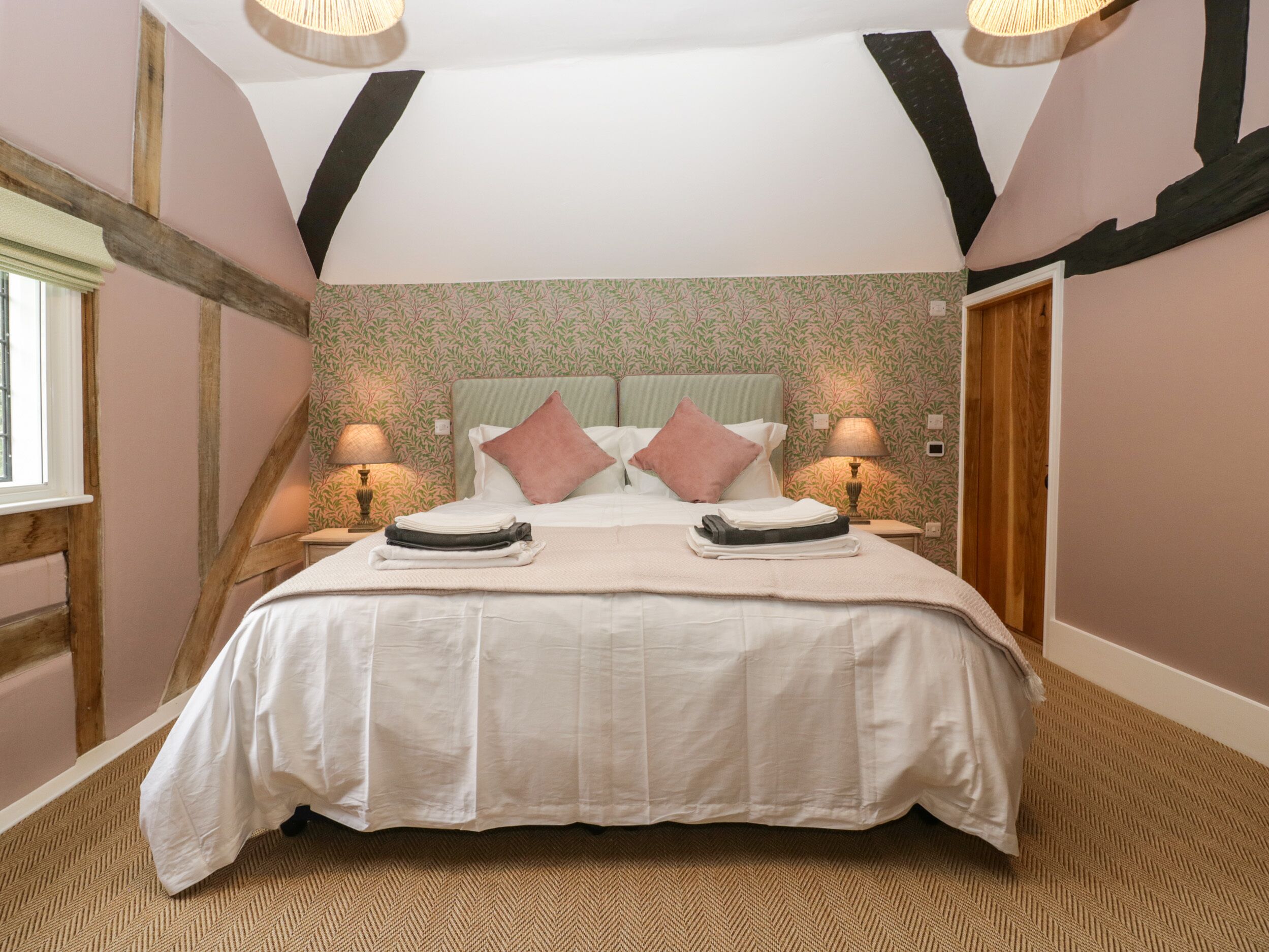 A bedroom with a large bed, two bedside tables with lamps, a window, and a door.
