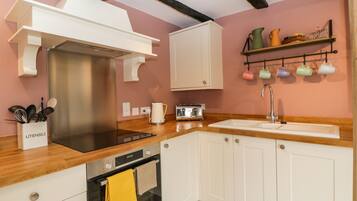 A modern kitchen with white cabinetry, a stainless steel range hood, a built-in oven, a wooden countertop, and a wall-mounted shelf with colorful mugs.