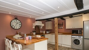 Una cocina moderna con una isla de madera, taburetes blancos tipo bar, lavadora integrada y un reloj en la pared.