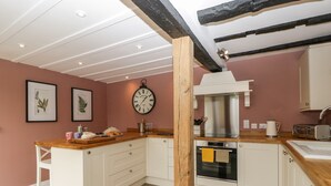 Una cocina con armarios blancos, encimera de madera, campana extractora de acero inoxidable y un reloj en la pared.