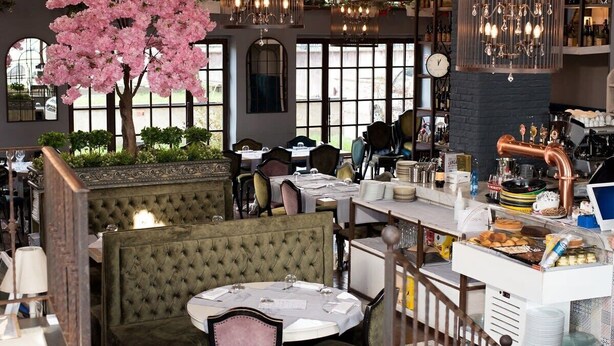 En restaurang med runda bord, bekväma sittplatser, en bardisk och ett stort fönster med utsikt.