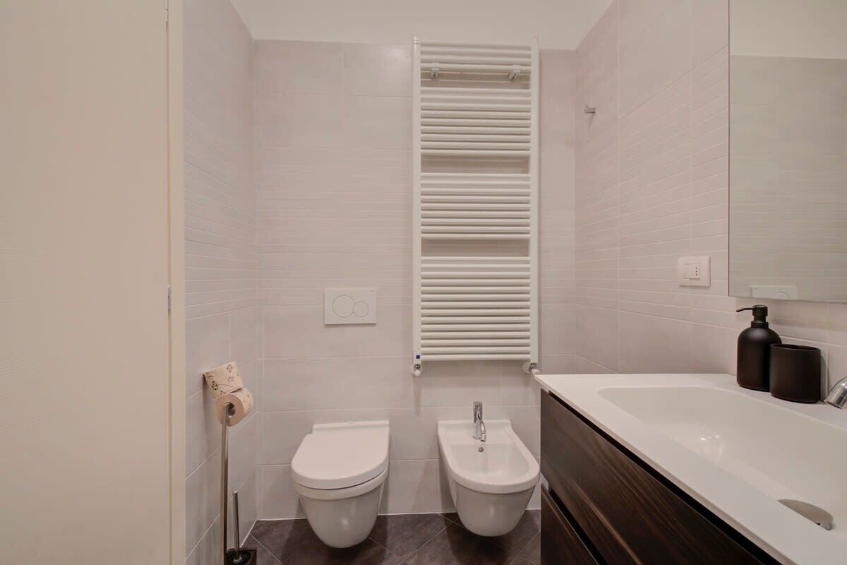 Een moderne badkamer met twee toiletten, een bidet, een witte wastafel en een handdoekhouder.