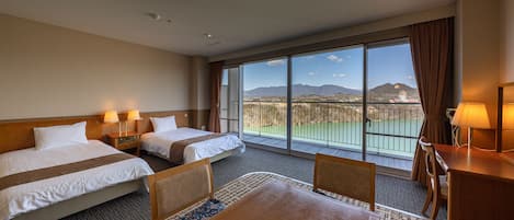 Ett hotellrum med två sängar, ett matbord och ett stort fönster med utsikt över berg och en golfbana.