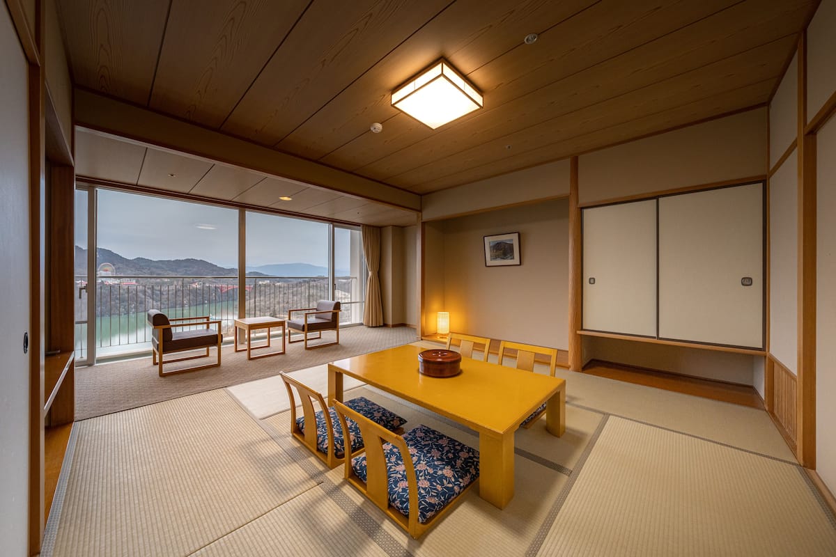 Una habitación tradicional japonesa con suelo de tatami, una mesa de madera baja y vistas a la ciudad a través de amplias ventanas.