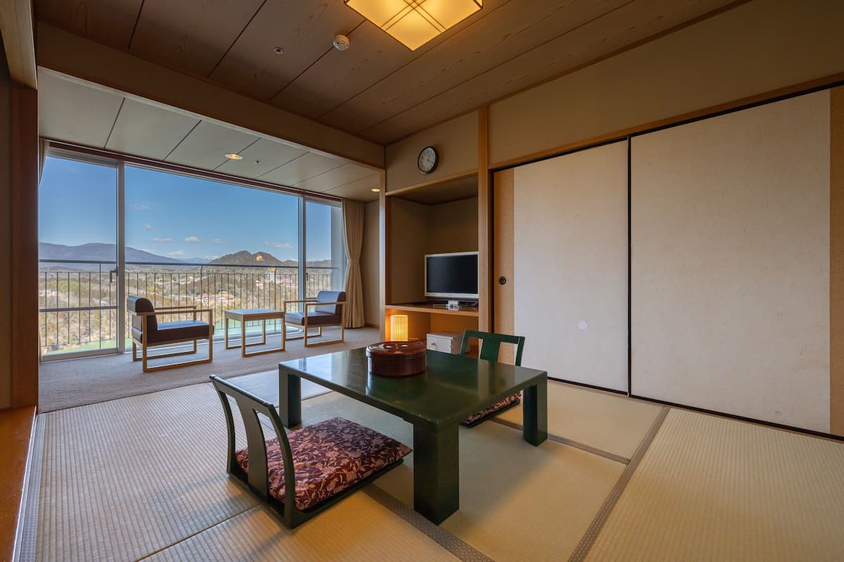Una habitación con esteras de tatami, una mesa baja, sillas, televisor y vistas a la montaña.