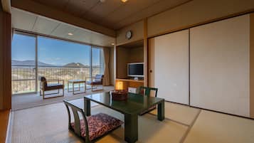 Een kamer met tatami matten, een lage tafel, stoelen, een televisie en uitzicht op bergen.