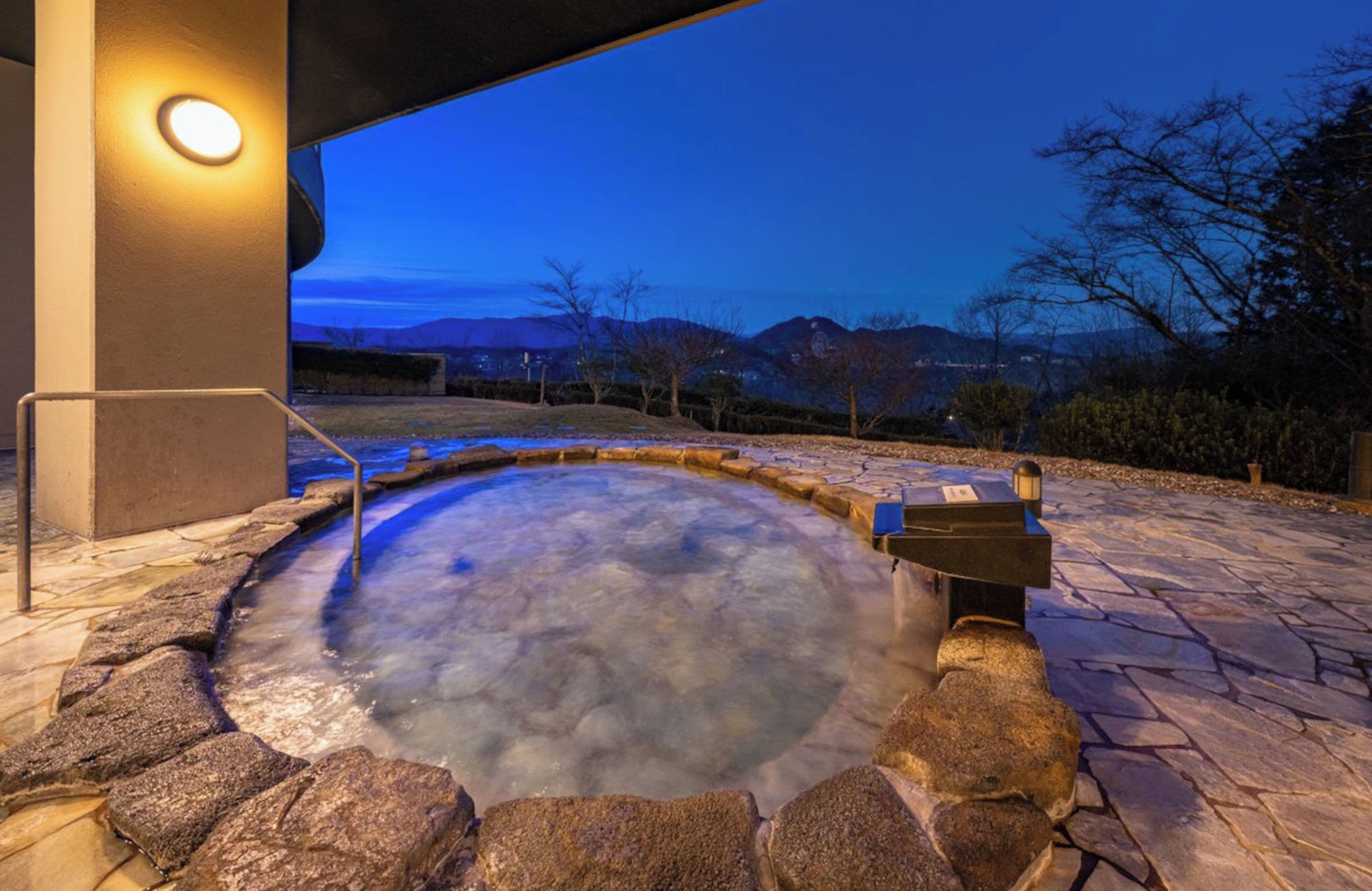 Ein Whirlpool mit Steinrand, einer Metallbank und Blick auf Berge im Hintergrund.
