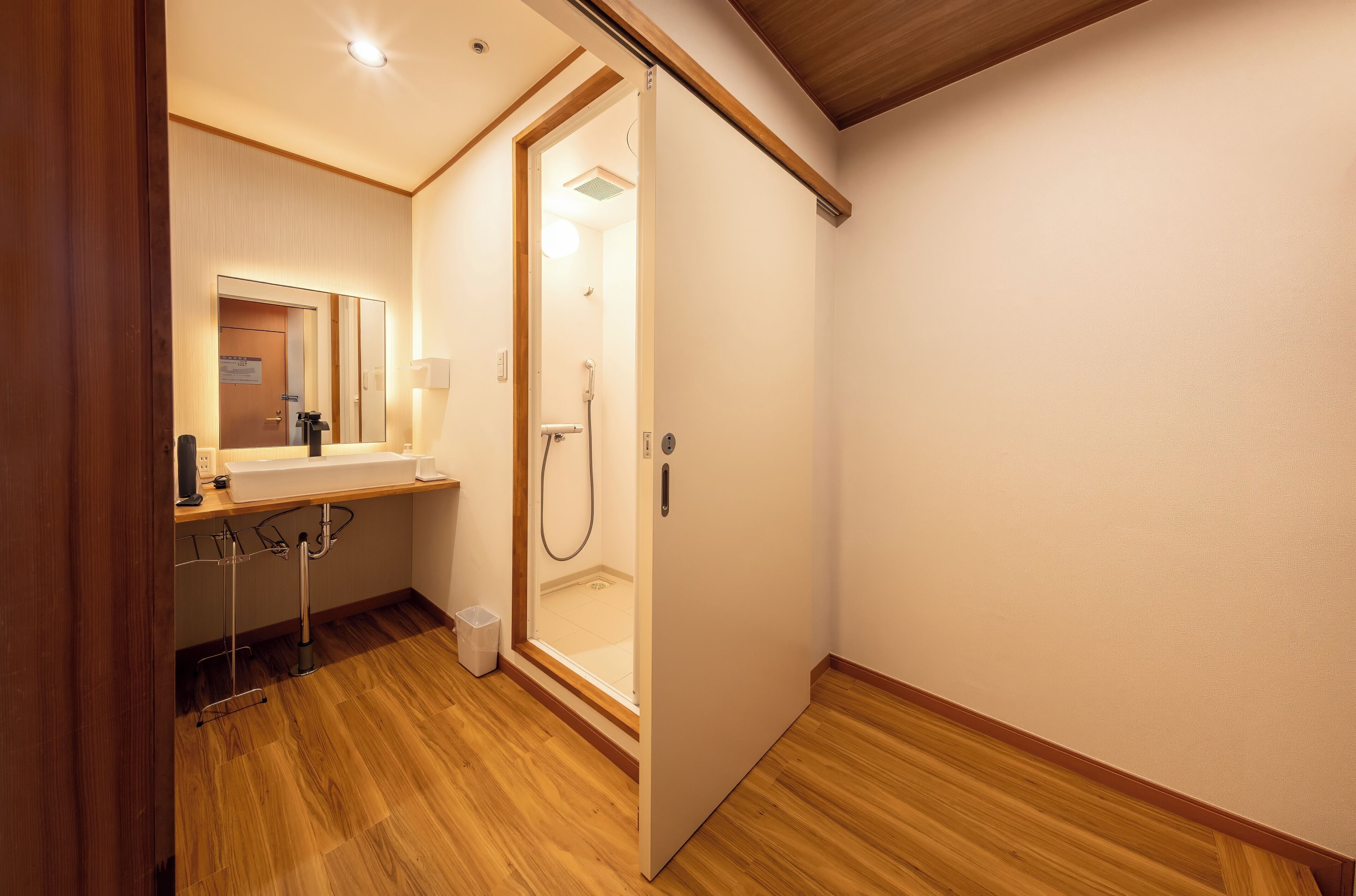 A compact bathroom with a wooden floor, a sink, a mirror, and a shower.