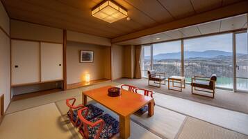 Ein traditioneller japanischer Raum mit Tatami-Böden, einem niedrigen Holztisch und Blick auf eine Stadtlandschaft durch große Fenster.