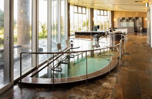 Ein Wellnessbereich mit einem runden Whirlpool, Glasgeländern und Blick ins Freie.