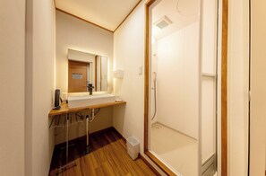Un baño con piso de madera, lavamanos, espejo y ducha.