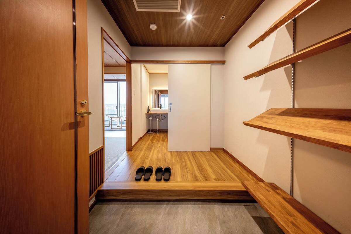 Un pasillo con piso de madera, una puerta a la izquierda y un zapatero a la derecha.