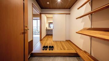 A hallway with wooden flooring, a door on the left, and a shoe rack on the right.