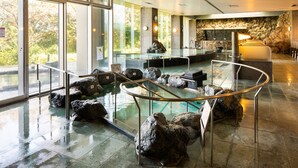 Zona d'una piscina interior moderna amb parets de vidre, una paret de pedra i una recepció.