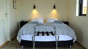 A bedroom with a bed, two bedside tables, a chair, and two wall-mounted lights. - Cottages built for privacy and unobstructed views (Bláskógabyggð)