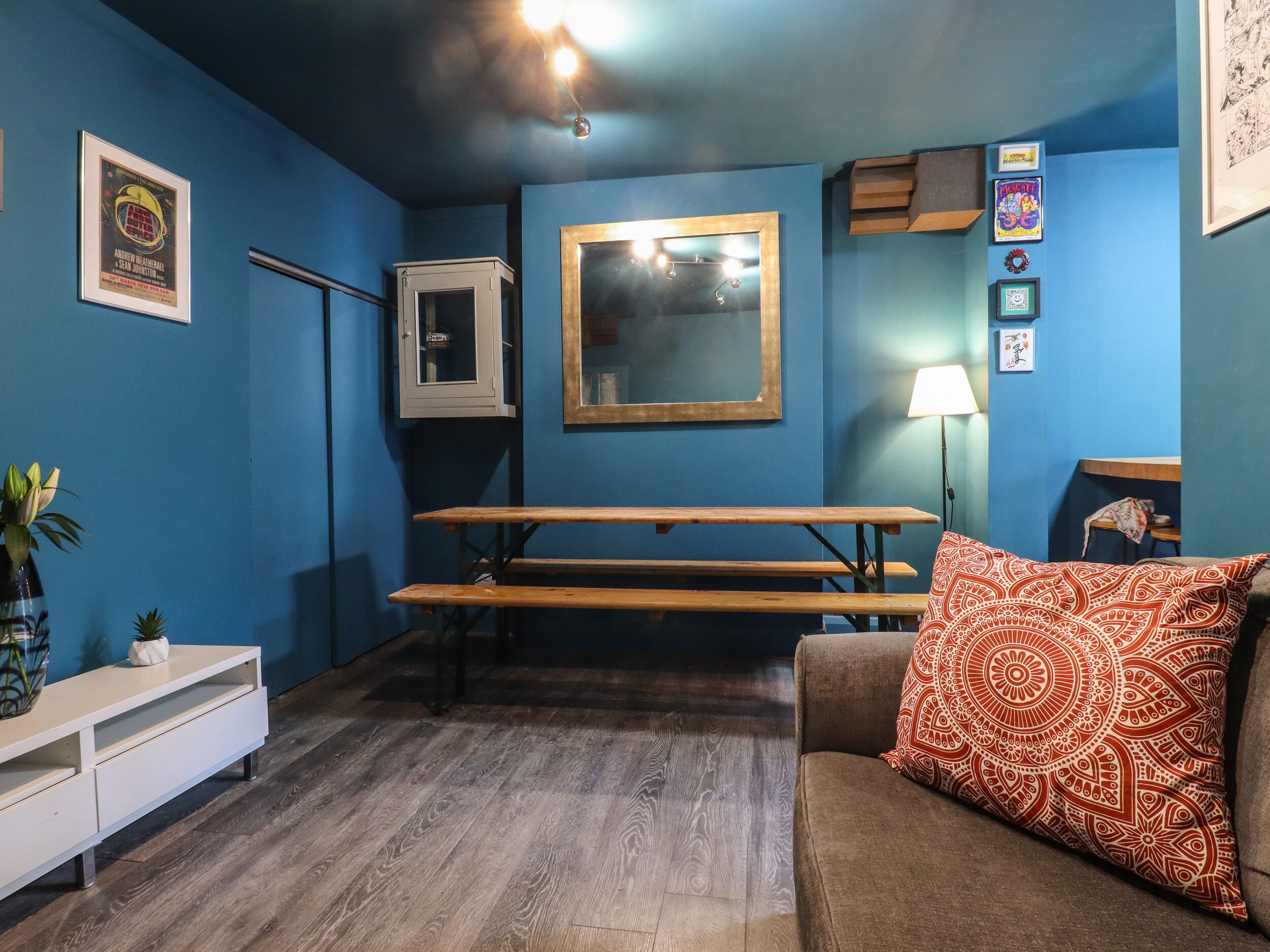 A room with blue walls, a wooden bench, a sofa with a patterned cushion, a small table, and a cabinet.
