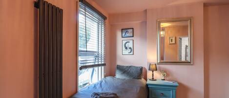 A bedroom with a bed, a nightstand, a mirror, and artwork on the wall.