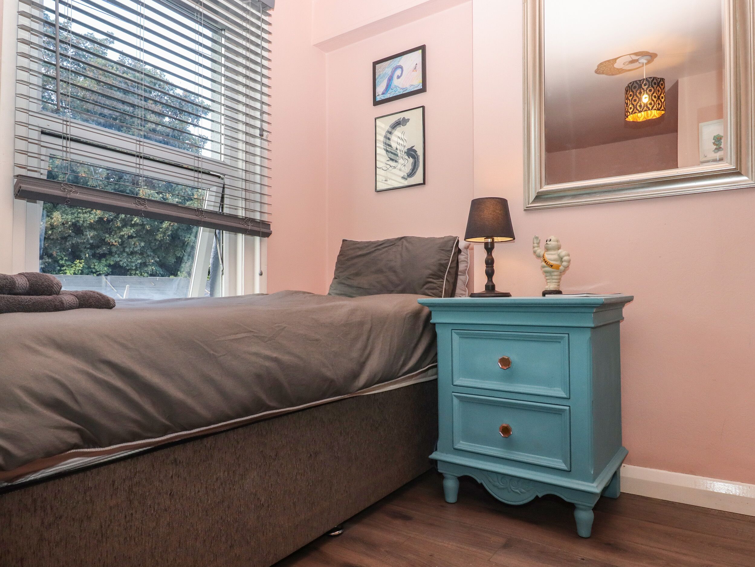 Una camera da letto con un letto, un comodino con lampada, una cassettiera e due quadri appesi al muro.