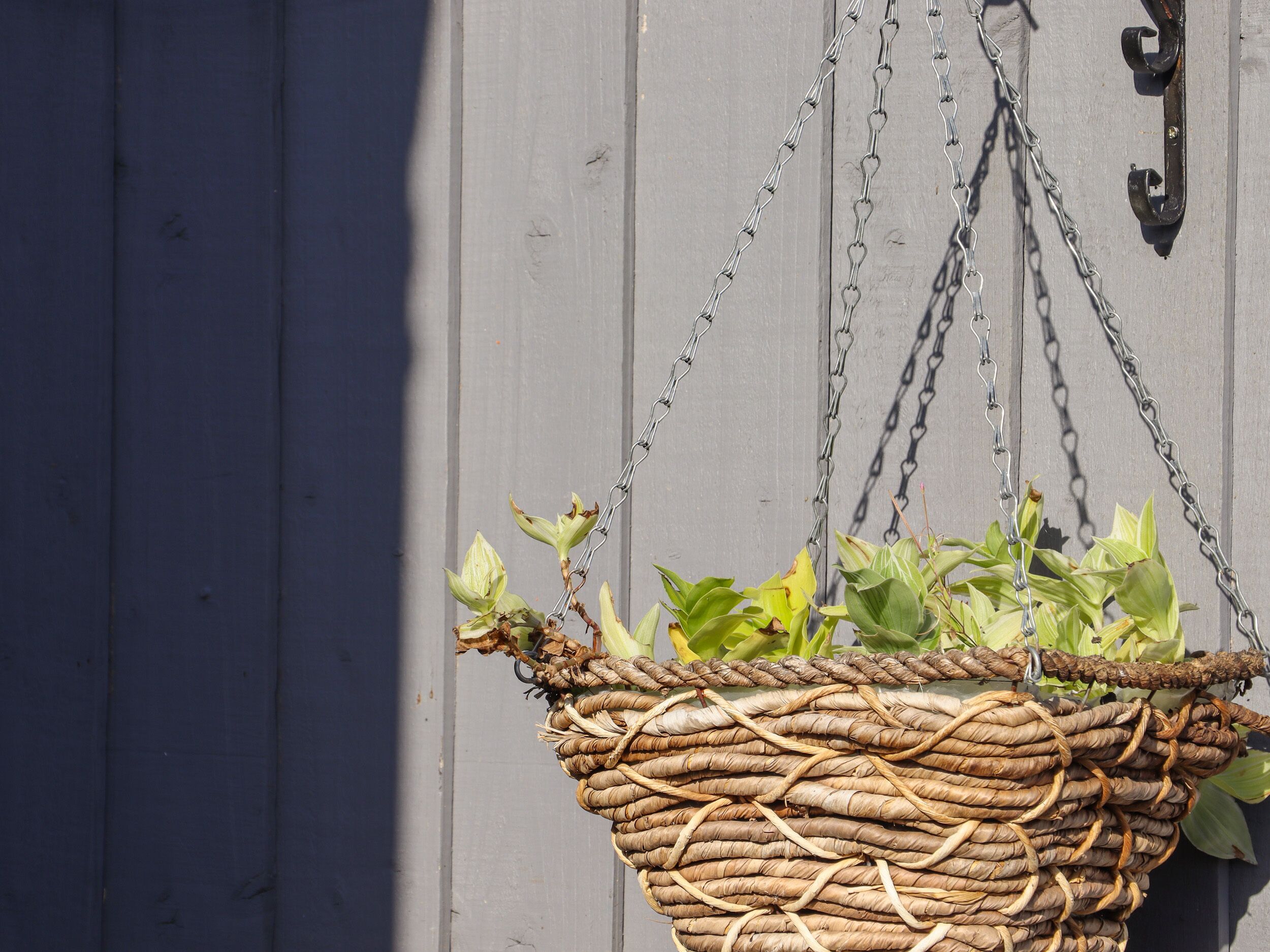 A woven basket hanging from a chain against a wooden wall.