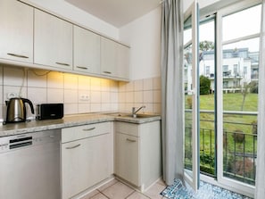 Eine moderne Küche mit hellen Schränken, einem eingebauten Geschirrspüler, einem Wasserkocher und einem Toaster. Ein großes Fenster bietet Blick auf eine Wohngegend.