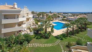 A residential area with a swimming pool surrounded by palm trees and a clear view of the sea.