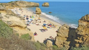 A beach with rocky cliffs, clear blue water, and people sunbathing.