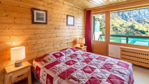 A wooden cabin bedroom with a bed, a nightstand, a lamp, and a window with a mountain view.