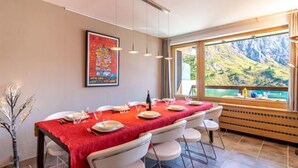 A dining area with a red tablecloth, white chairs, and a painting on the wall.