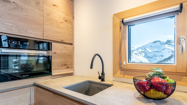 A modern kitchen with wooden cabinets, a built-in oven, a sink, and a window with a mountain view. - Home Club (Lavachet) by Interhome (Tignes)