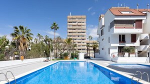 Une piscine à l’eau d’un bleu cristallin, entourée d’un bâtiment blanc doté de balcons et de palmiers.