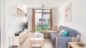 Un salon moderne avec un canapé, une table basse, un téléviseur et une vue sur l’extérieur.