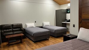 Quarto com duas camas, um sofá, um banco de madeira e uma pequena mesa.