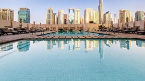 Una piscina en la azotea con agua cristalina, rodeada de sillas de descanso y sombrillas, con un horizonte urbano de fondo.
