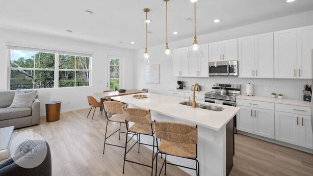 A modern kitchen with white cabinetry, a central island with bar stools, stainless steel appliances, and pendant lighting. - 1052 3BR Luxury Resort House by Disney Orlando (Davenport)