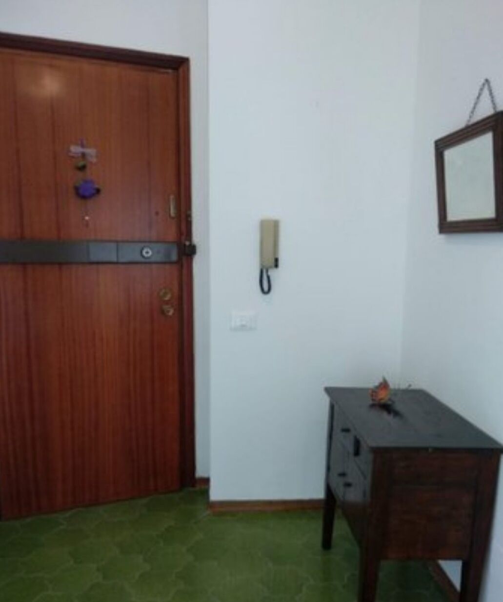 A room with a wooden door, a desk with drawers, a telephone, and a framed picture on the wall.