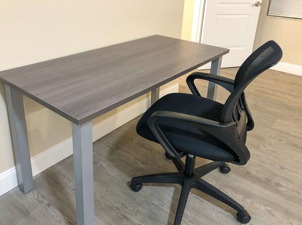 A room with a dark wooden desk and a black office chair with a mesh backrest.