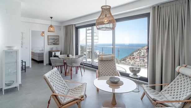 Una habitación de hotel moderna con balcón, ventanas amplias y zona de comedor.