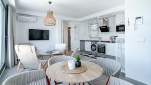 Una cocina moderna con armarios blancos, horno empotrado y microondas. Cuenta con un comedor con mesa de vidrio y sillas acolchadas.